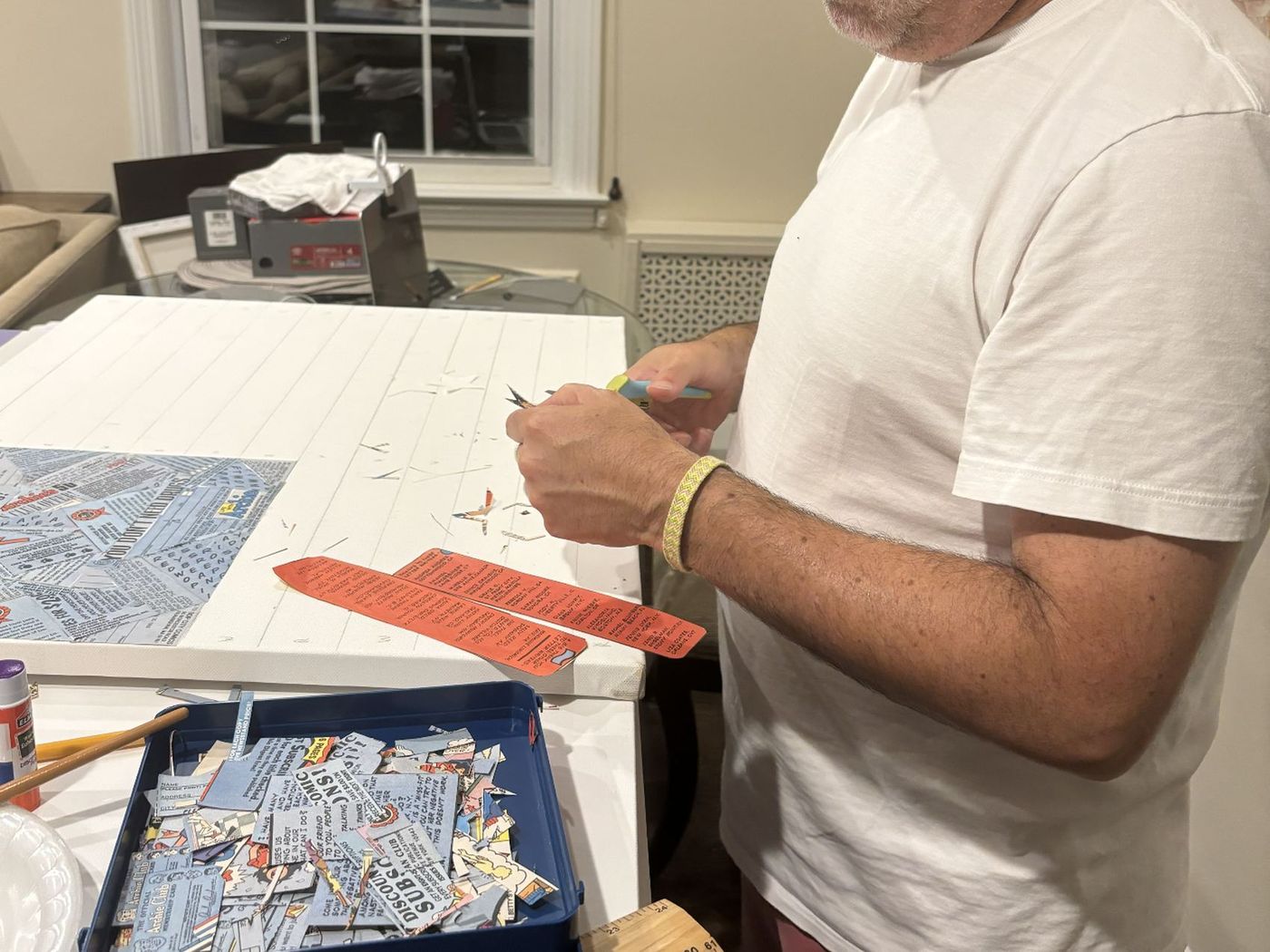 Cutting a strip of comic by hand at the canvas, beside a tray of fragments